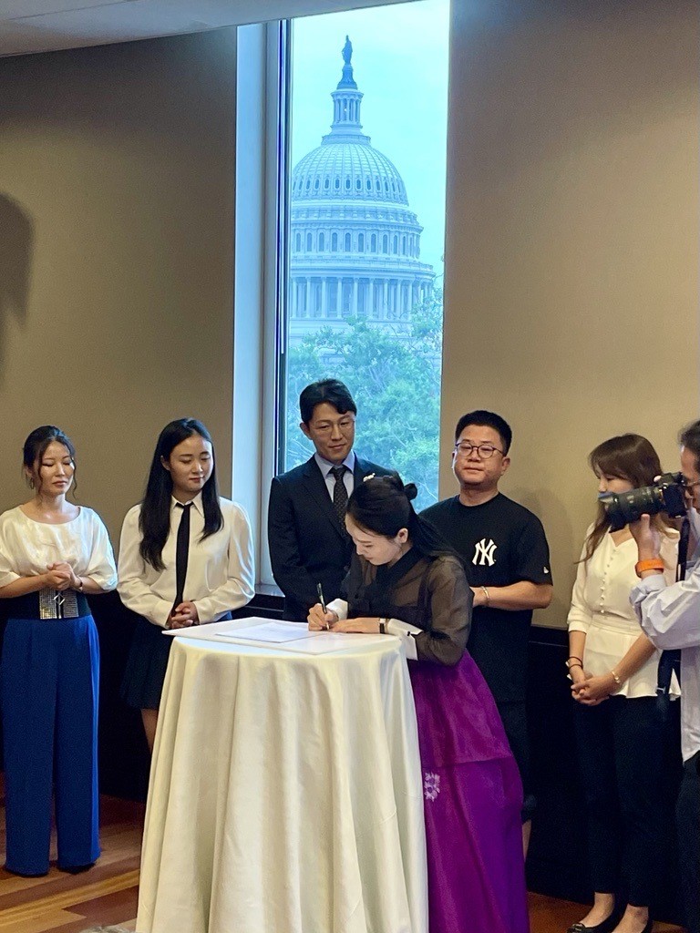 North Korean defectors signing a statement of unity at a table.